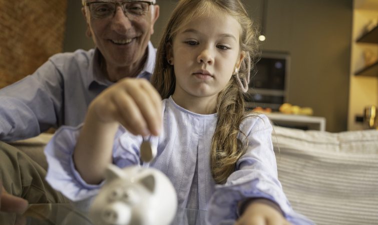 Grandfather and granddaughter saving coins in a piggy bank, learning financial literacy